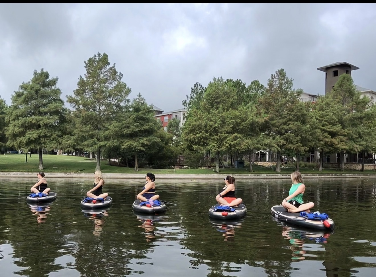 A private SUP yoga group seated on paddleboards along the water in The Woodlands — mobile events for groups